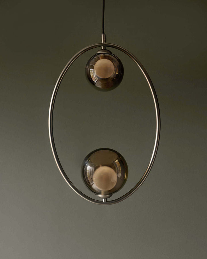 A modern pendant light with two spherical, smoked-glass lamps encased in a metal hoop, suspended from the ceiling.