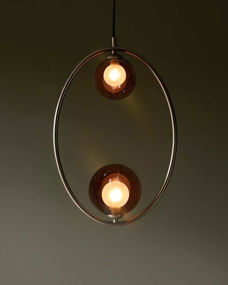Oval pendant light with two amber glass globes suspended within a brushed metal frame. Modern lighting fixture.