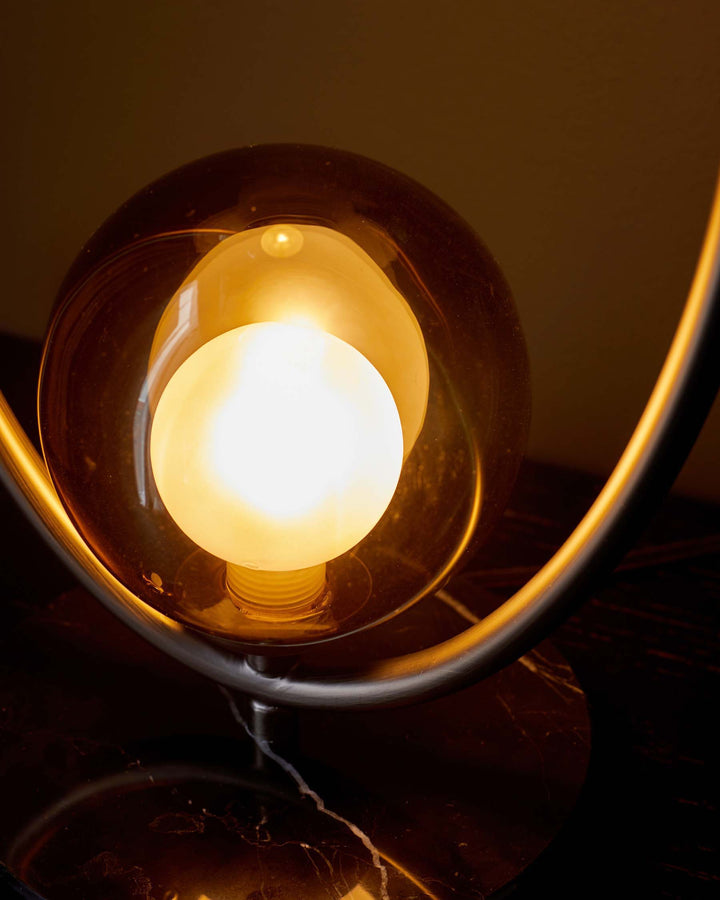 Stylish lamp with a spherical bulb, encased in glass and mounted on a sleek, curved metal frame. Marble base.