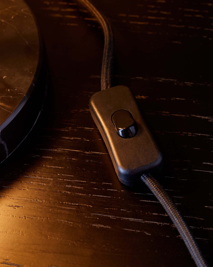 A close-up of a dark wood table with a black electrical cord and a switch. The table has a glossy finish.