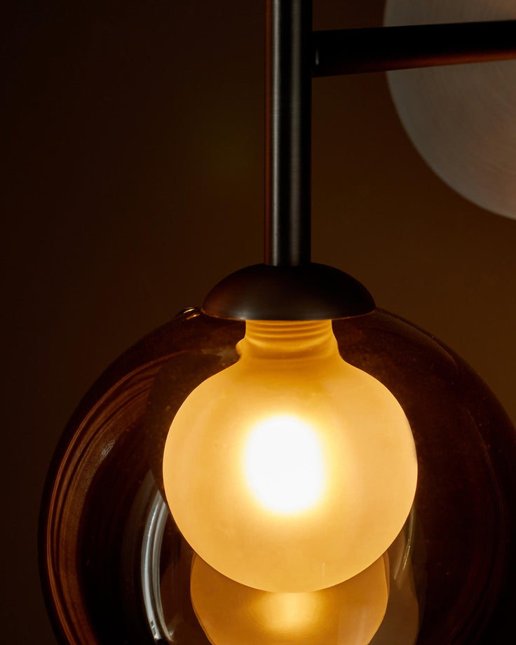 Close-up of a striking modern pendant light with a frosted bulb and a tinted glass shade, creating a warm glow.