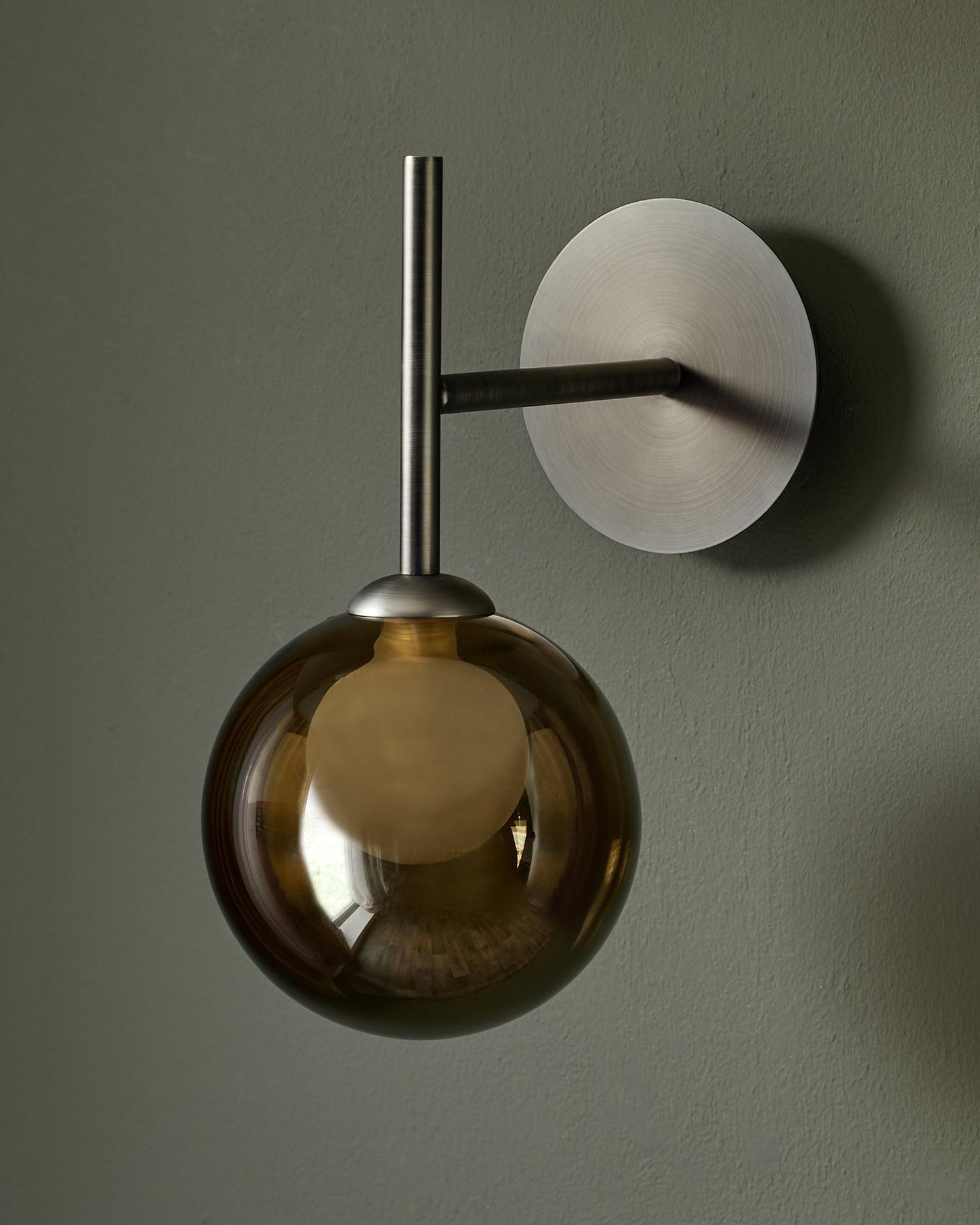 A stylish globe wall light with smoked glass and brushed metal finish. Provides a warm and modern aesthetic.