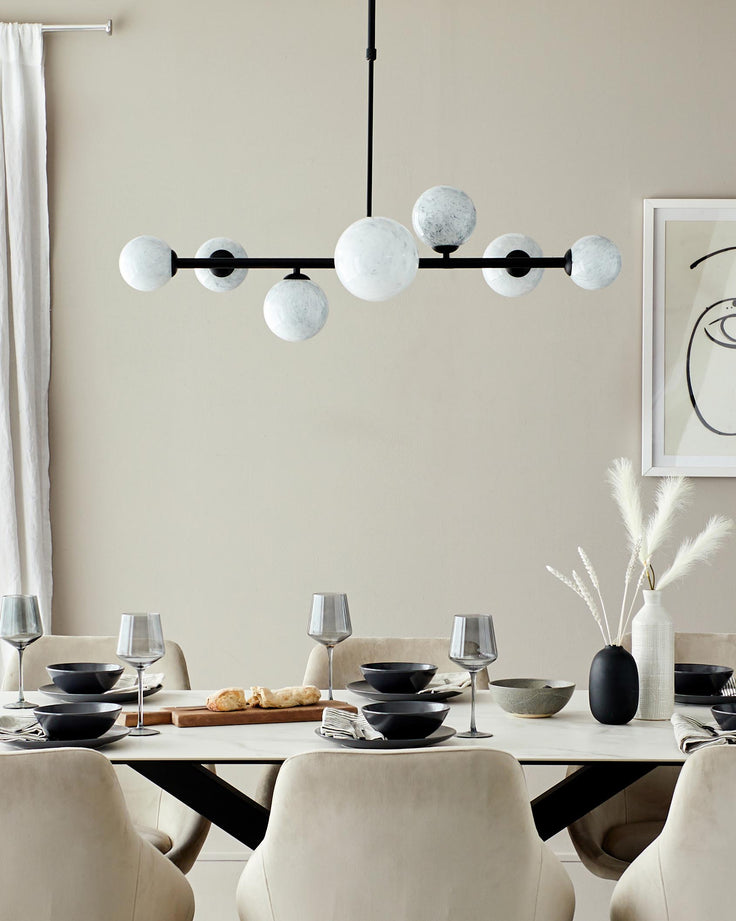 Modern dining table with a beige finish, paired with plush chairs, elegant glassware, and a stylish chandelier above.