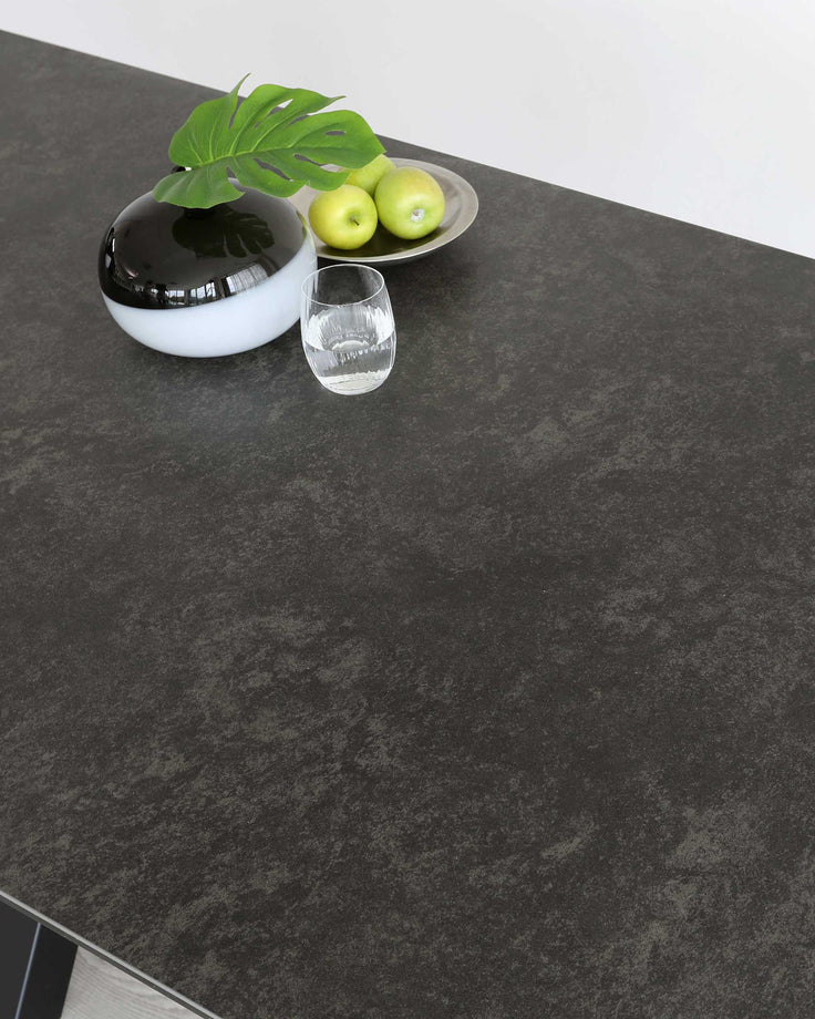 A sleek black tabletop with a decorative bowl, fresh apples, a clear glass, and a vibrant green leaf for a modern touch.