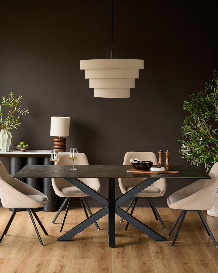 Riley 8-seater dining table in dark grey ceramic with black metal X-frame base, styled with beige chairs and pendant light.