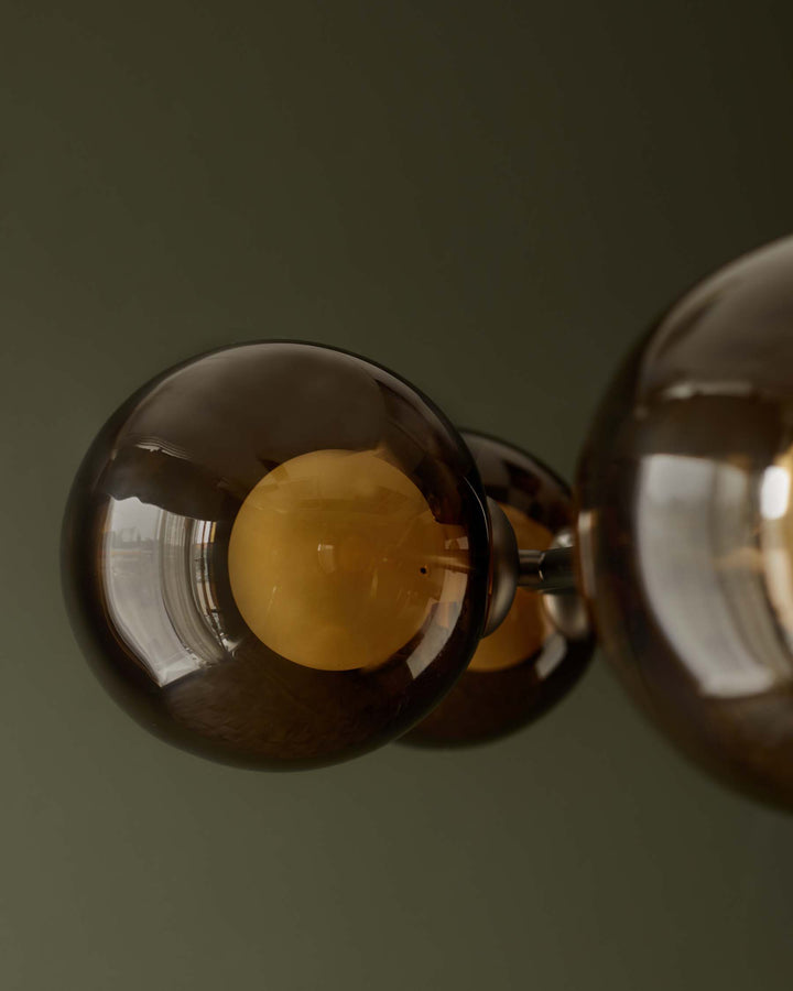 A contemporary ceiling light fixture with tinted glass globes and brass fittings against a muted green background.