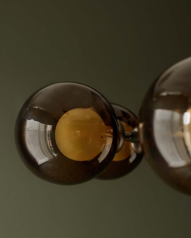 A contemporary ceiling light fixture with tinted glass globes and brass fittings against a muted green background.