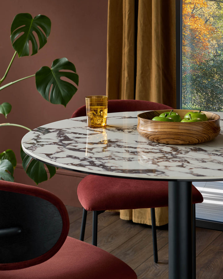 A modern dining table with a marble effect top and accompanying red chairs.