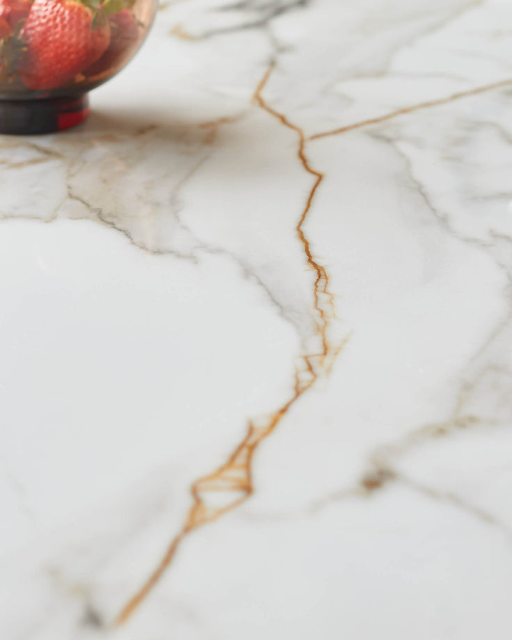 Light marble surface with brown veins, and bowl of strawberries in the top left corner.