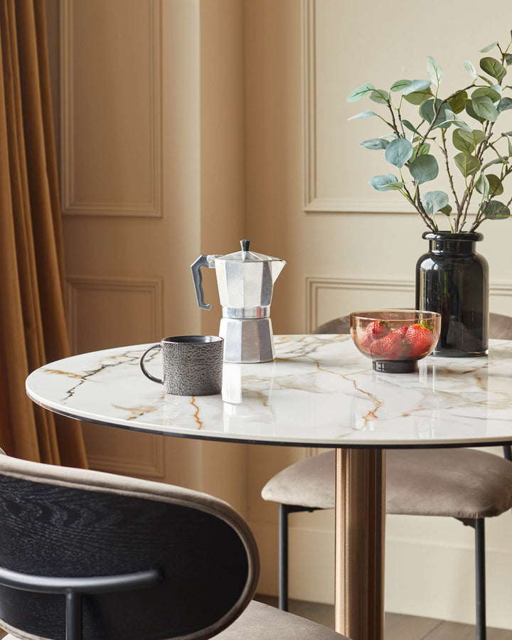 A stylish round marble table with coffee maker, mug, vase and a bowl of strawberries. Chairs complete the look.