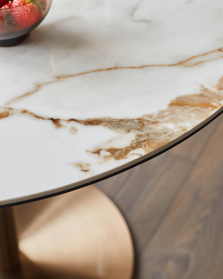 Close-up of a round marble-effect table with a metallic base and a bowl of strawberries on top, sitting on a wooden floor.