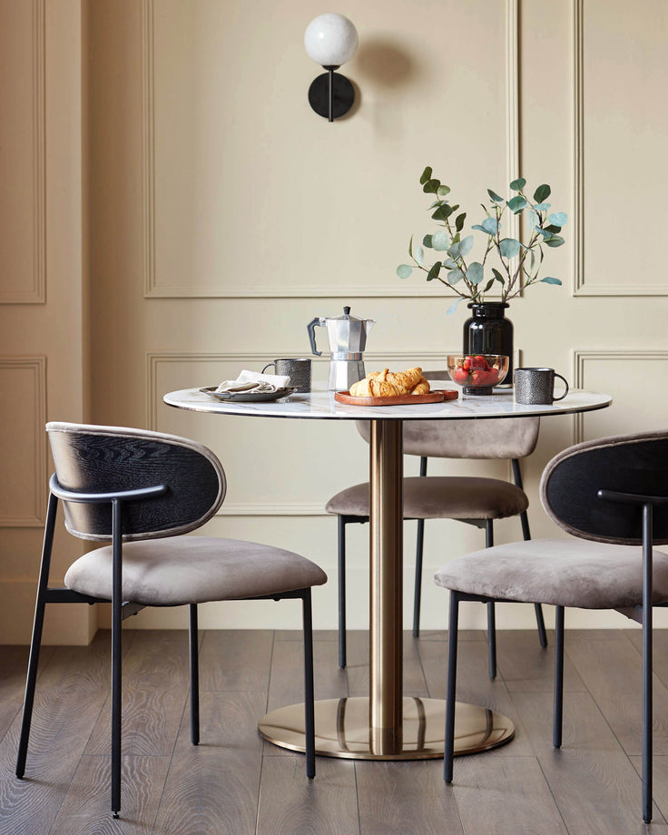 Dining area with round marble table, gold pedestal base, and three modern chairs with velvet seats.