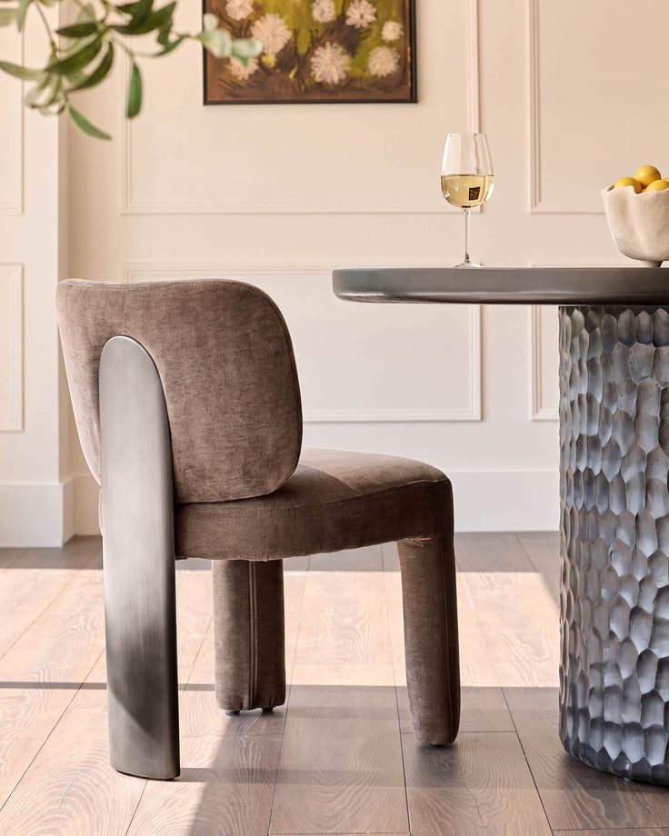 Rosalie dining chair in mocha fabric with curved backrest, shown at round Grey table with white wine glass.