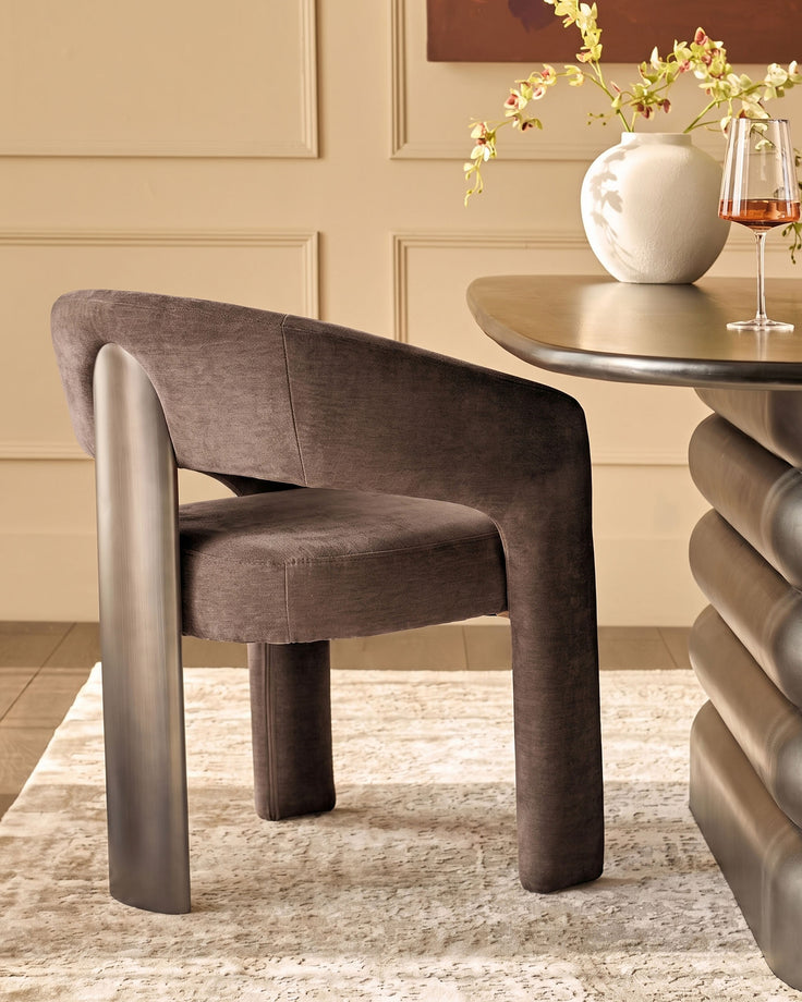 Rosalie dining armchair in mocha fabric with curved arms and cylindrical legs, shown at round table with wine glass and floral arrangement.