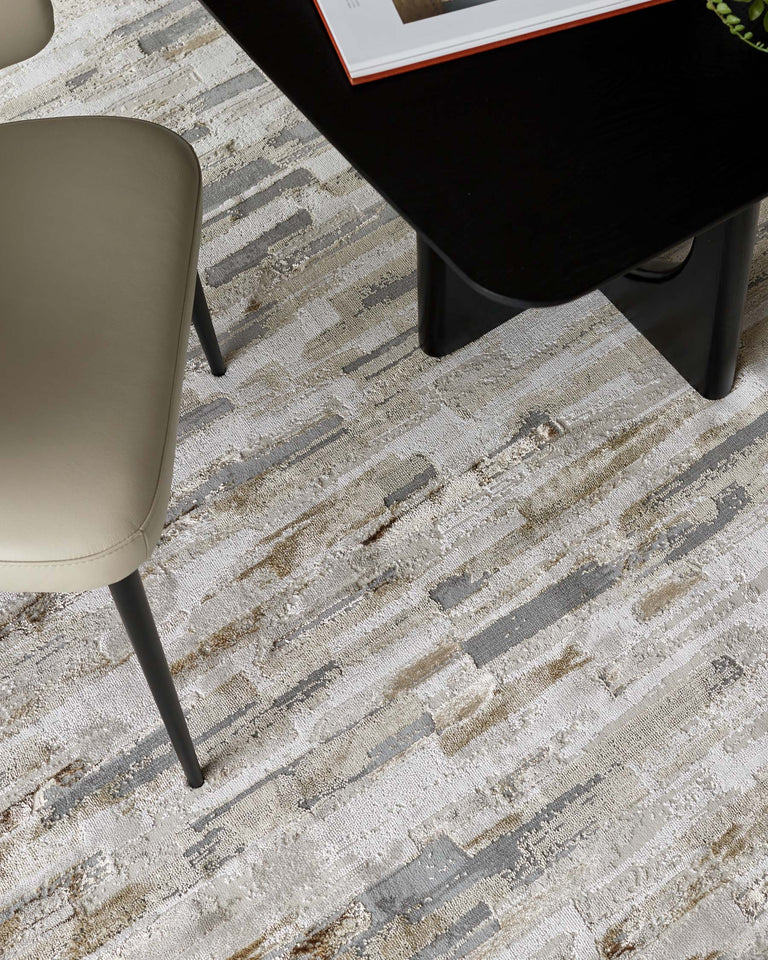 Contemporary beige upholstered chair with black metal legs and a sleek black coffee table with a curved edge design resting on an abstract-patterned area rug in neutral tones.