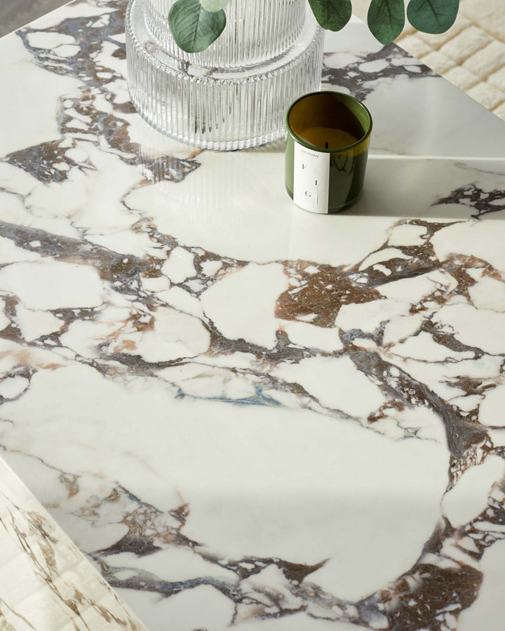 Close-up of a marble table surface with a candle and vase. The marble has white, brown and grey veining.