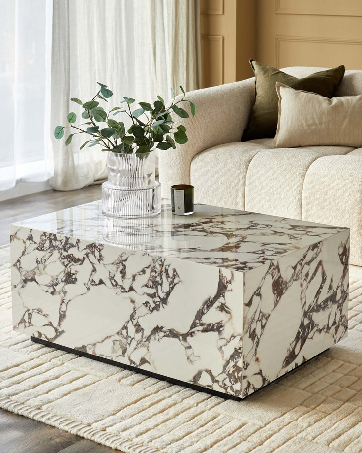 A modern living room with a marble coffee table, stylish sofa and cushions, alongside a decorative vase and candle.