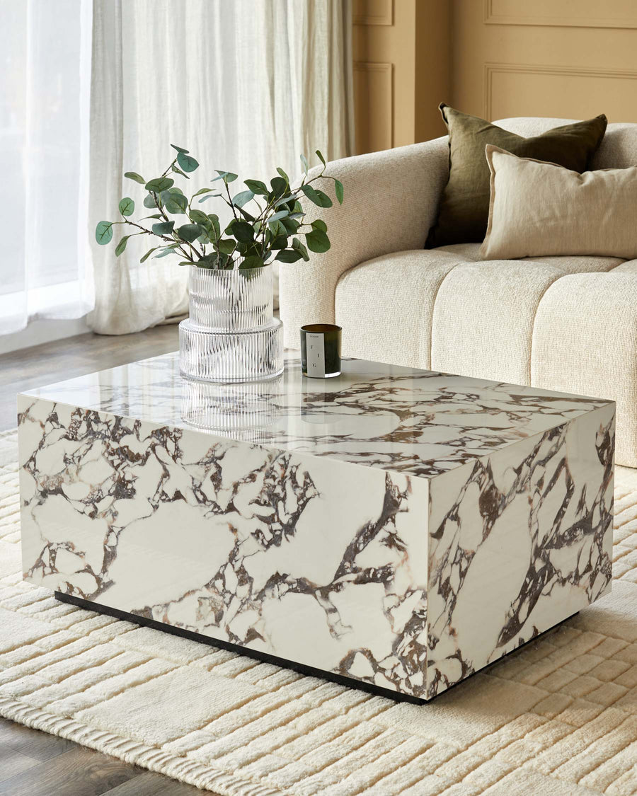A modern living room with a marble coffee table, stylish sofa and cushions, alongside a decorative vase and candle.