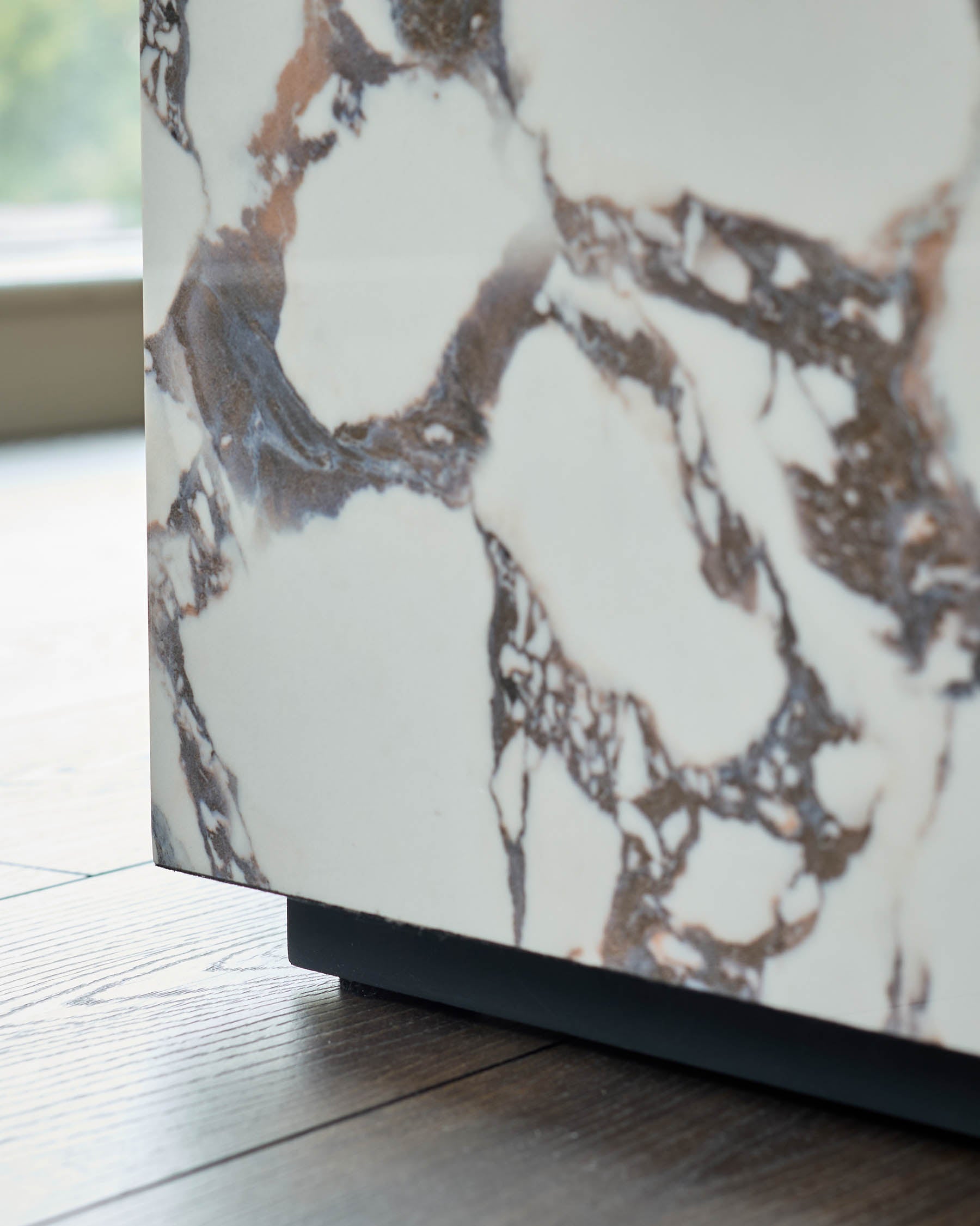 Close-up of a marble effect furniture piece with a dark base, sat on a wooden floor with natural light from a window.
