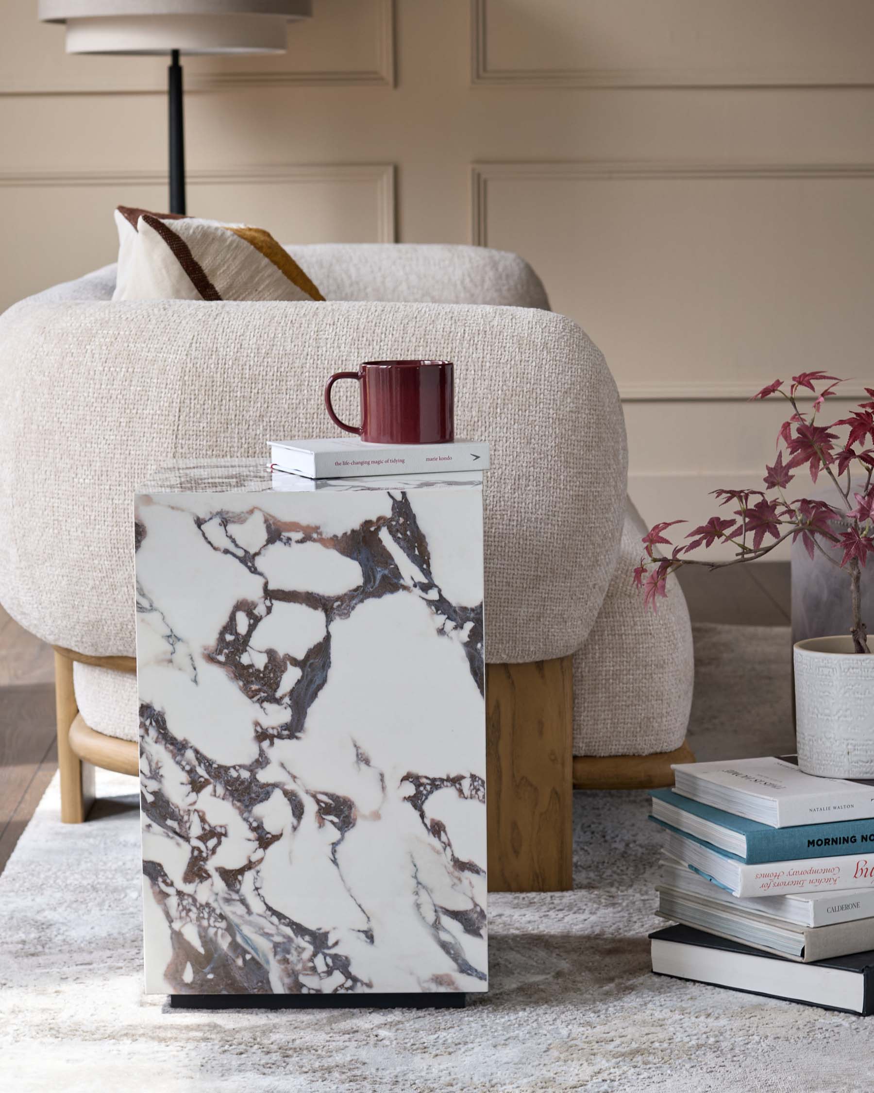 A stylish living room scene featuring an upholstered chair, marble side table, books and a decorative lamp.