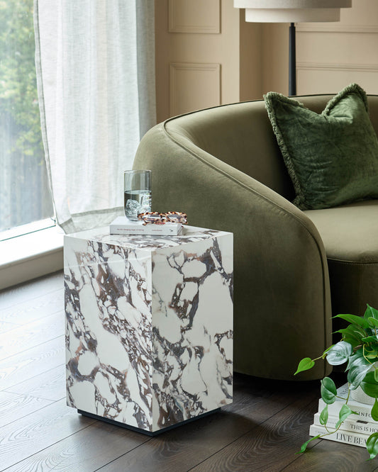 A contemporary living room featuring a marble side table, an olive green velvet sofa, and a stylish lamp.