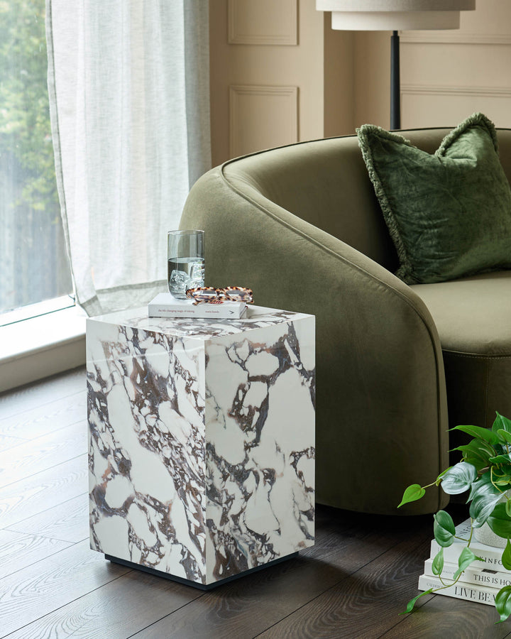 A contemporary living room featuring a marble side table, an olive green velvet sofa, and a stylish lamp.