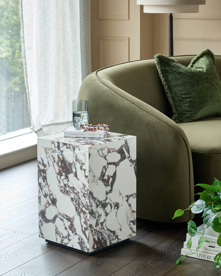 A contemporary living room featuring a marble side table, an olive green velvet sofa, and a stylish lamp.