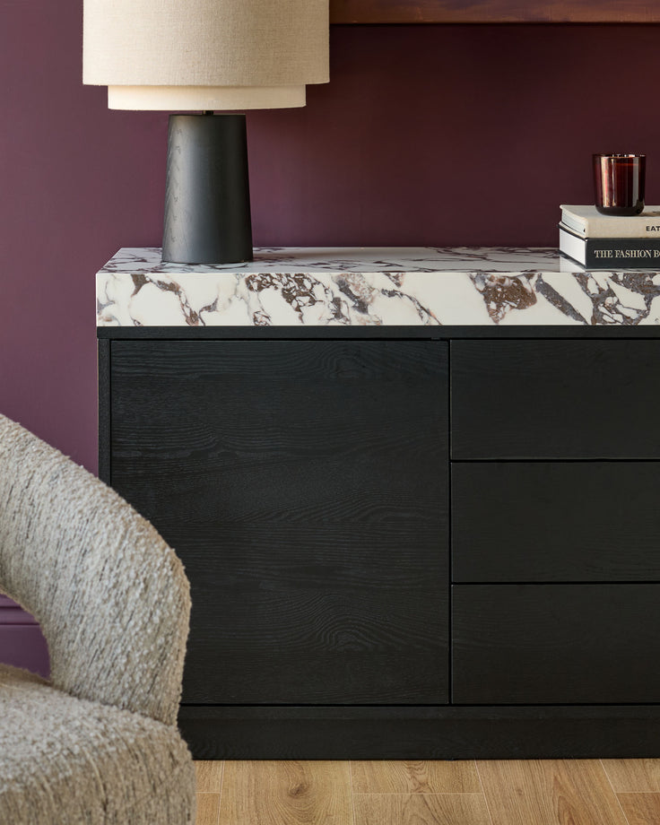 Russo sideboard in black wood with white Calacatta marble top, displayed in a styled bedroom setting with lamp and books.