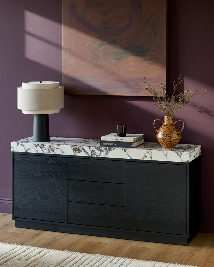 Russo sideboard in black wood with Calacatta white marble top, styled with lamp, books, and gold vase.