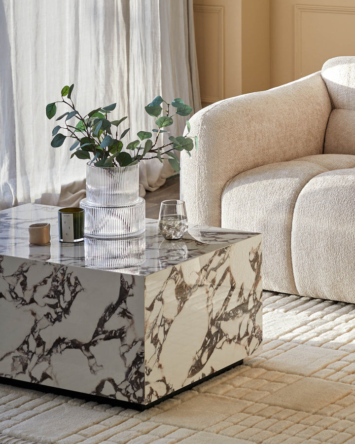 A contemporary living room setup with a marble coffee table, stylish glass vases and a comfy armchair on a patterned rug.