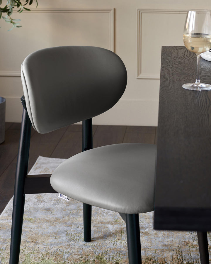 A grey dining chair with black wooden legs sits alongside a dark wooden table. A wine glass is on the table.