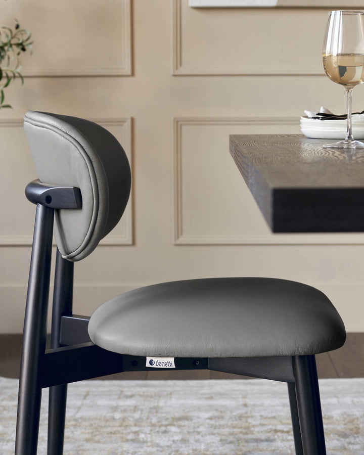 Close-up of a grey Danetti dining chair with dark wood frame, part of a table and wine glass in the background.