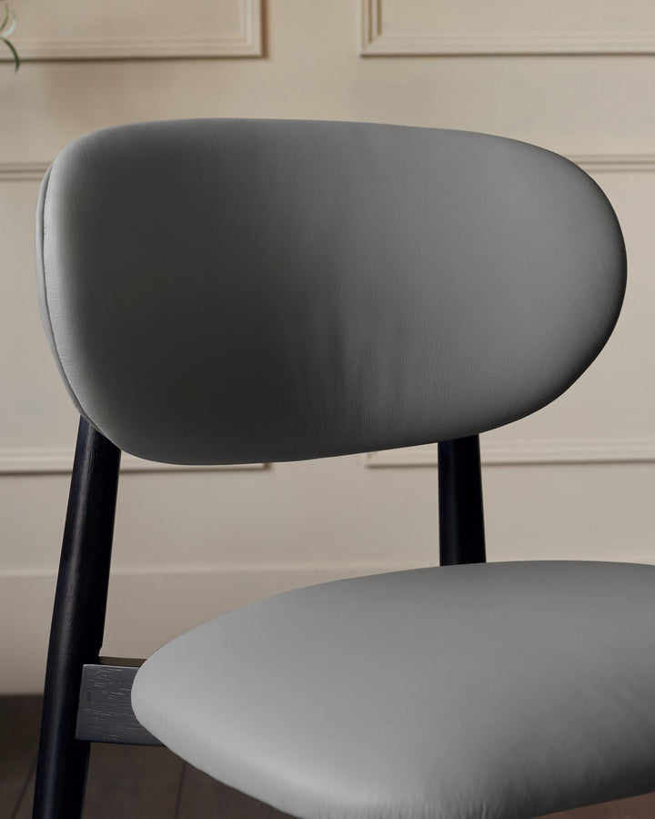 Close-up of a grey chair featuring a rounded backrest and black wooden legs. The design is modern and minimalist.