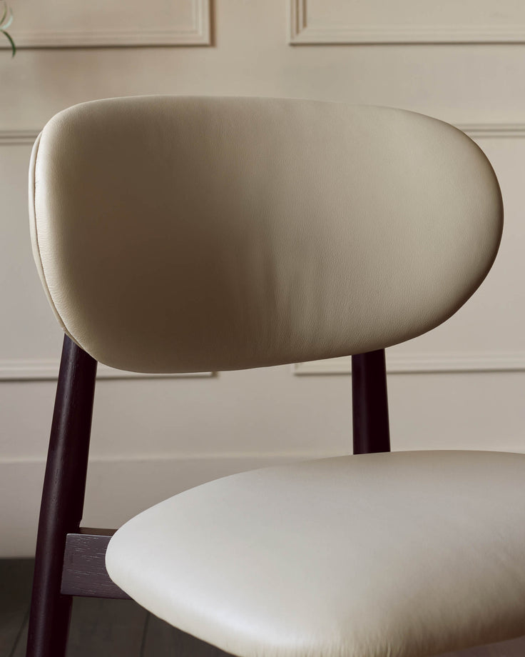 Close-up of a stylish chair with a cream seat and backrest, complemented by dark brown wooden legs.