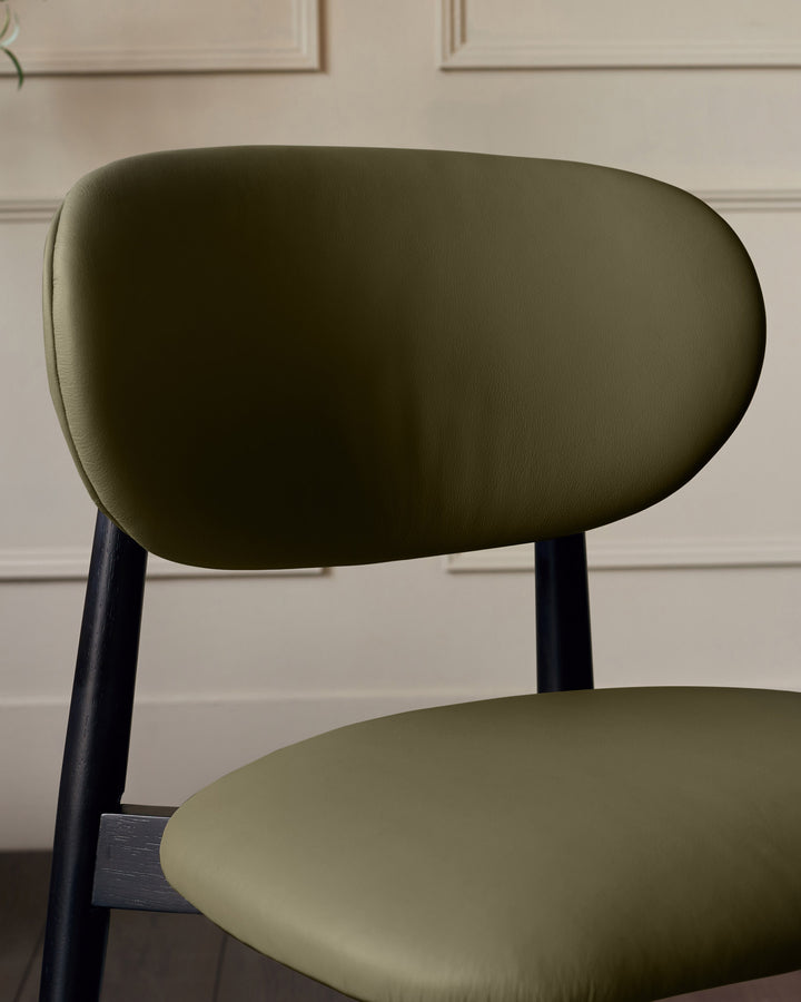 Ryann dining chair in olive green leather with dark wood legs, shown from a side angle highlighting the curved backrest and seat.