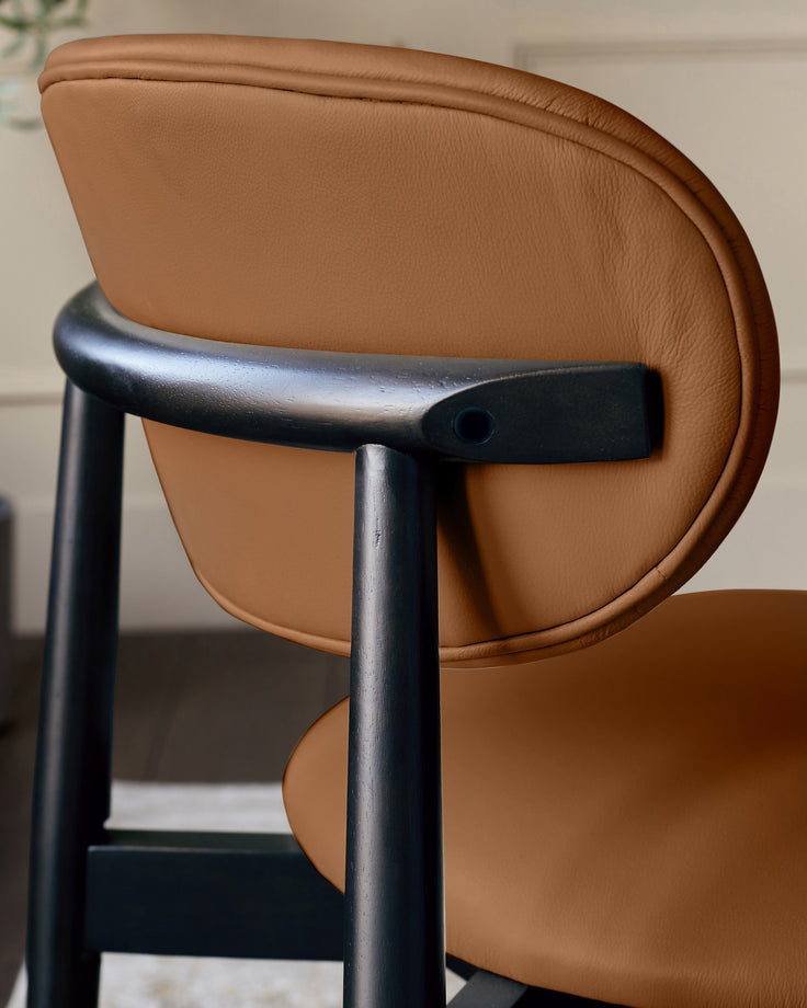 Ryann dining chair in tan leather with black metal frame, shown from side angle highlighting curved backrest and armrest detail.