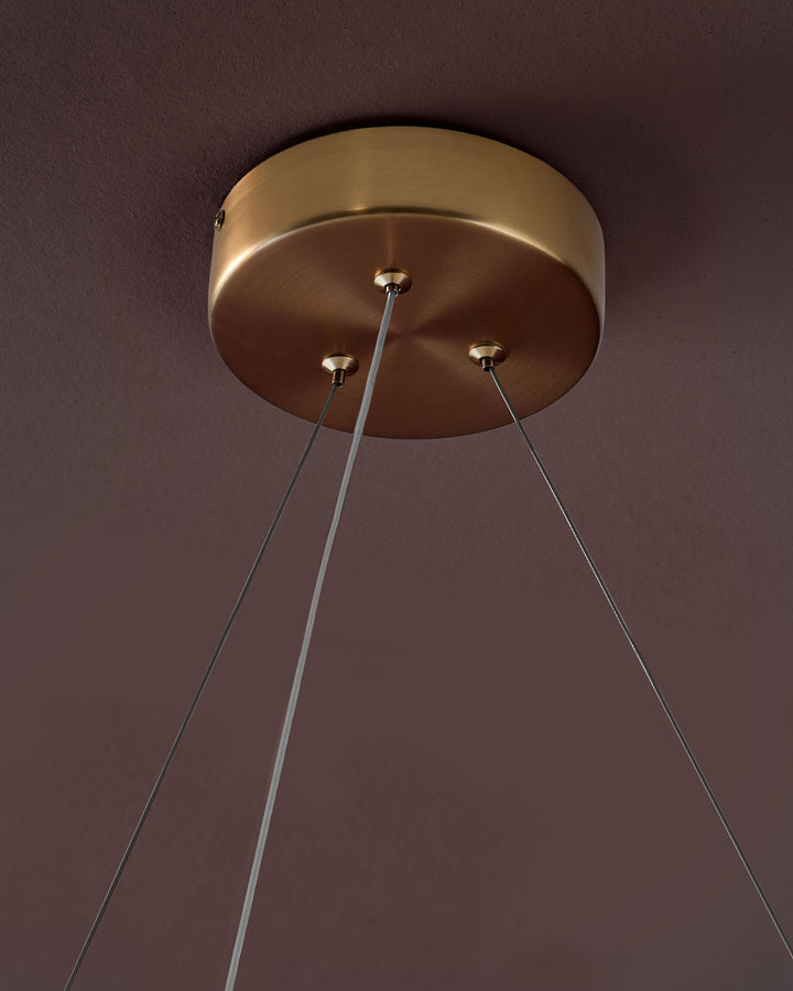 Sadie small pendant light with brass fixture and three thin cables against a mauve wall.
