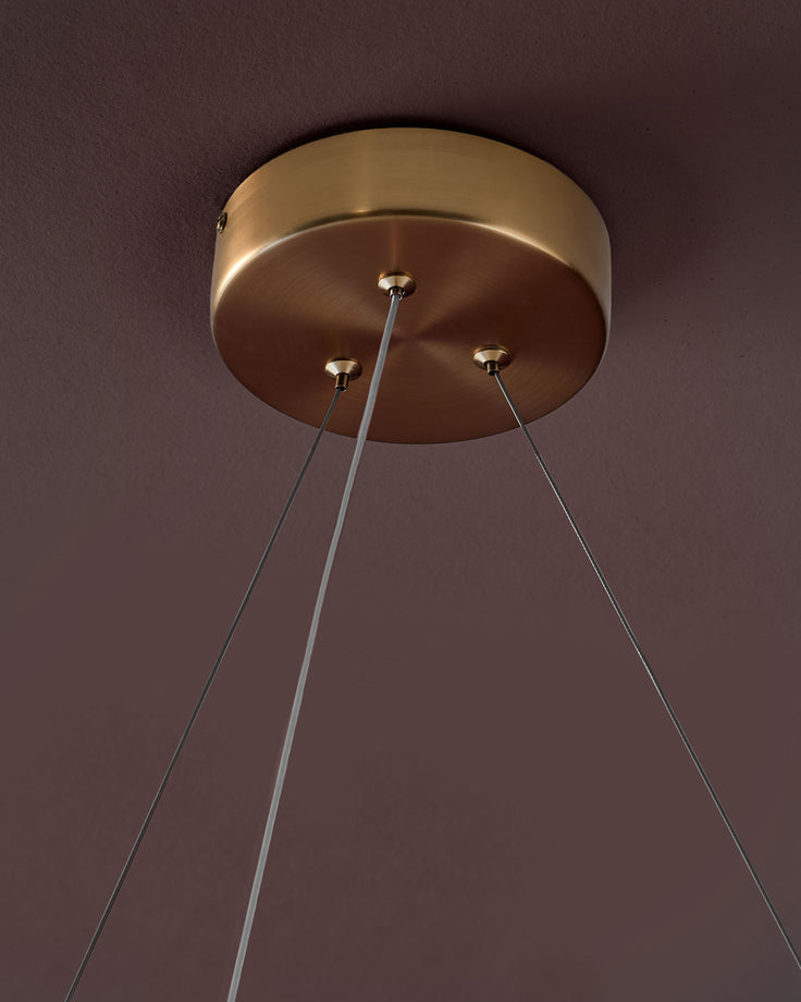 Sadie small pendant light with brass fixture and three thin cables against a mauve wall.