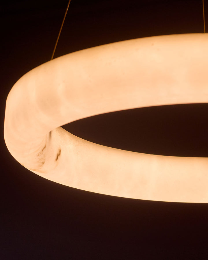 Sadie small pendant light in alabaster effect natural finish, shown from side angle with warm glow highlighting curved sculptural shape.