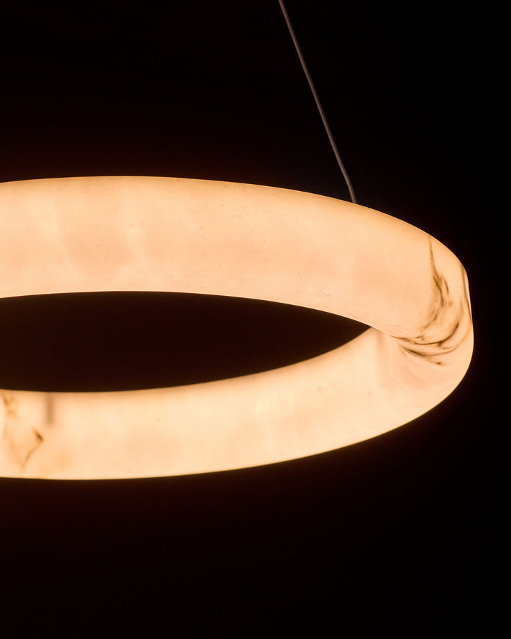 Sadie Small Pendant Light in alabaster effect natural finish, shown as a glowing rounded ring-shaped fixture against a dark background.