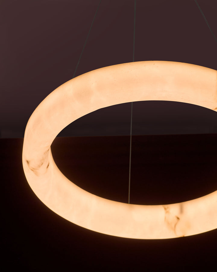 Sadie small pendant light in alabaster effect natural finish, showing glowing circular ring design suspended against dark background.