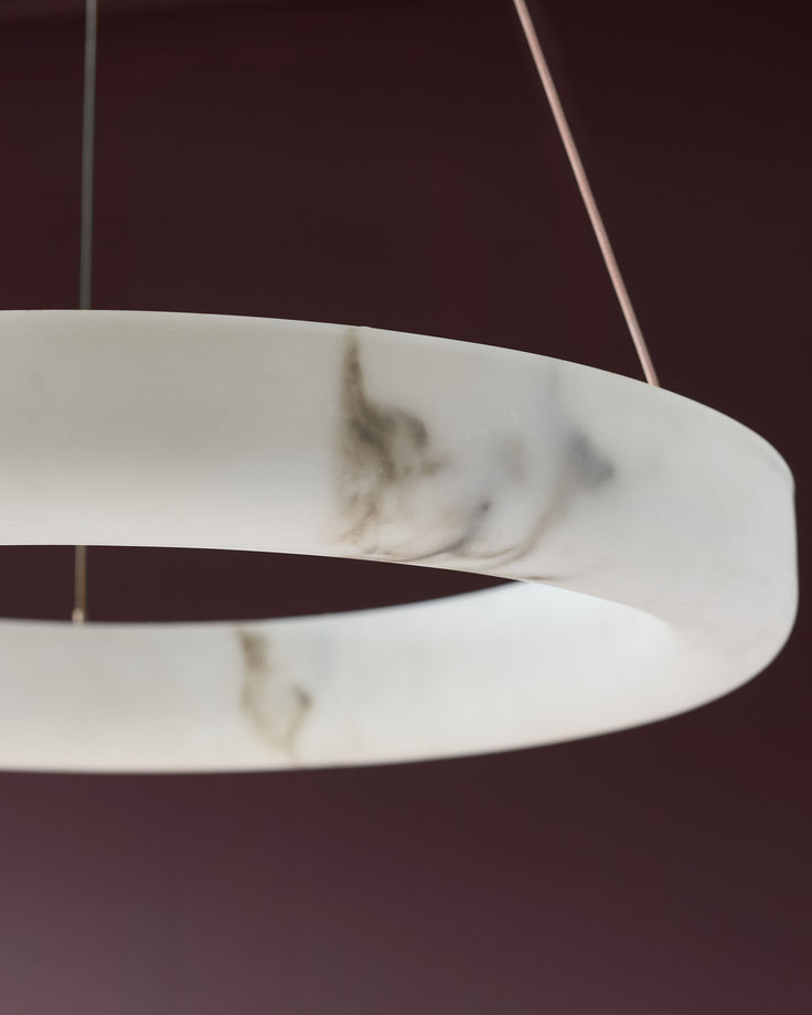Sadie small pendant light in alabaster finish, showing curved cylindrical shade with marbled pattern detail against burgundy background.