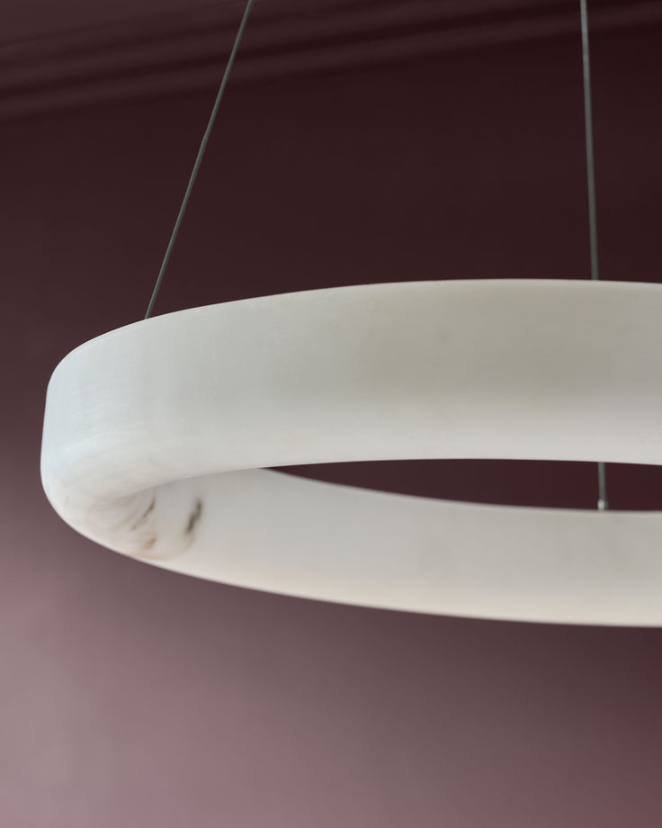Sadie small pendant light in alabaster finish, showing curved sculptural design and suspension cables against burgundy ceiling.
