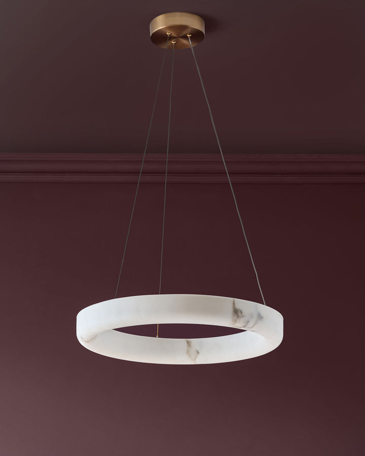 Sadie small pendant light in alabaster with brass fixture, suspended by three cords against a burgundy wall.