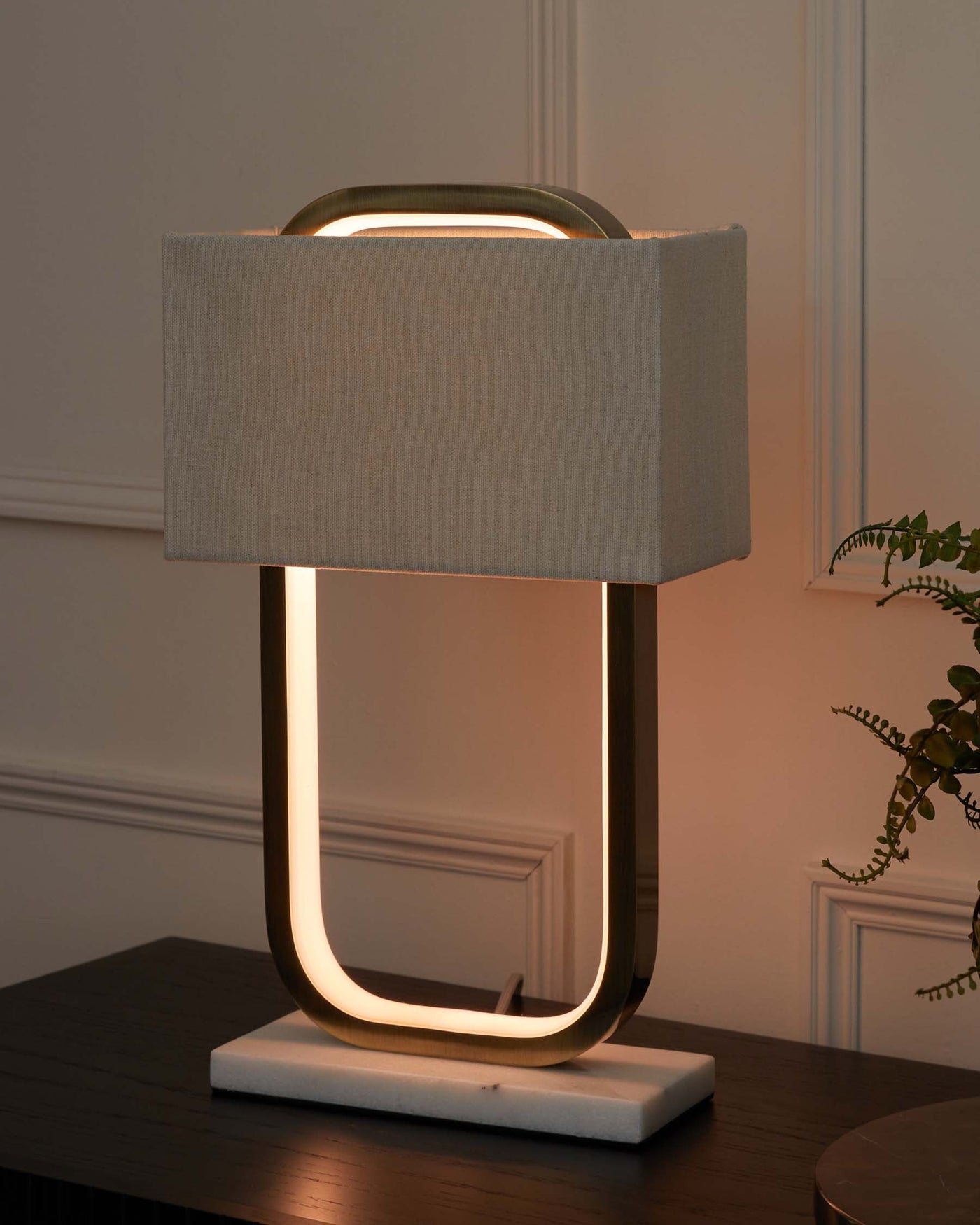 Modern table lamp with a unique geometric base featuring an illuminated open rectangular frame and a textured fabric shade.