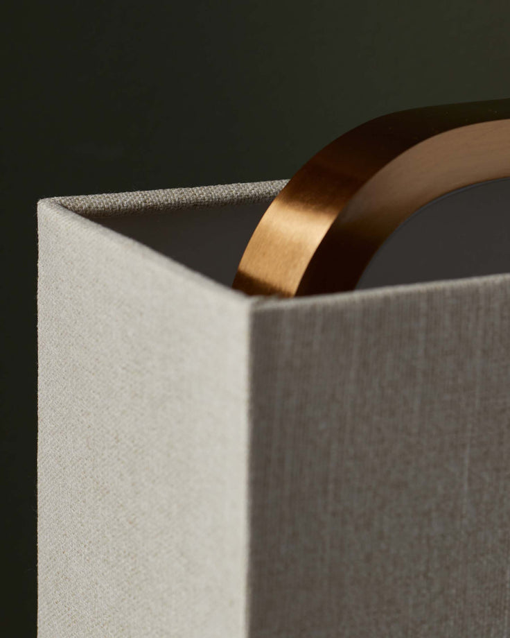 Close-up of a stylish lamp with a square shade and curved brass detail. Modern lighting for a contemporary home.