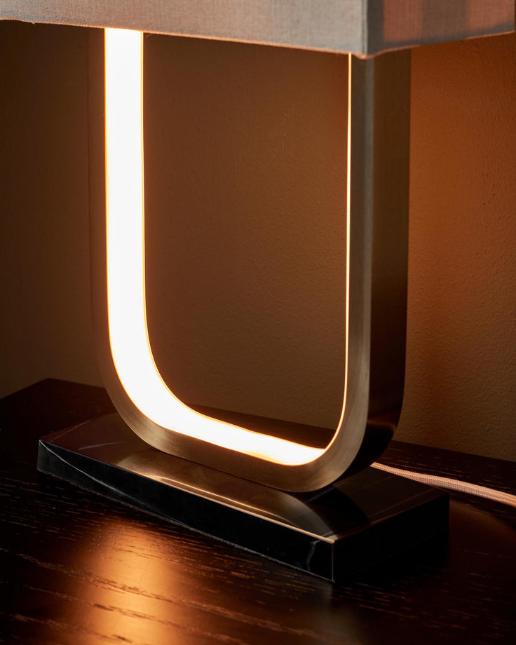 Modern U-shaped lamp with a black base, sat on a dark wooden table. The lamp's light casts a warm glow.