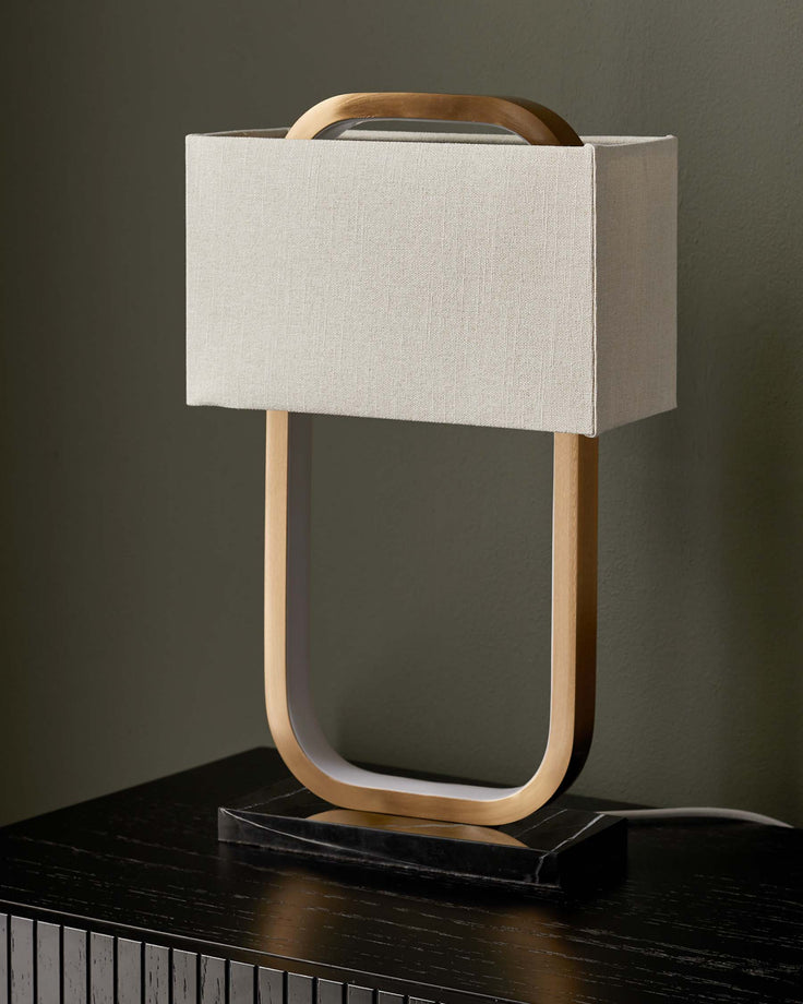 A lamp with a fabric shade and wooden frame sits on a black wooden dresser with vertical slat detailing.
