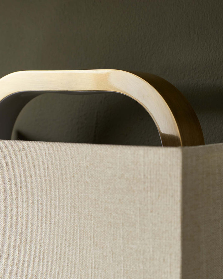 Close-up of a lamp with a gold handle and a neutral fabric shade against a muted green wall.