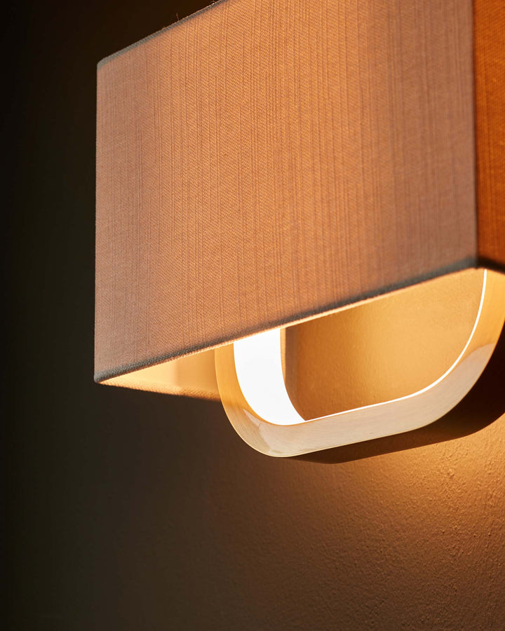 Close up of a stylish wall lamp with a fabric shade and a warm, glowing light, casting shadows on the wall.